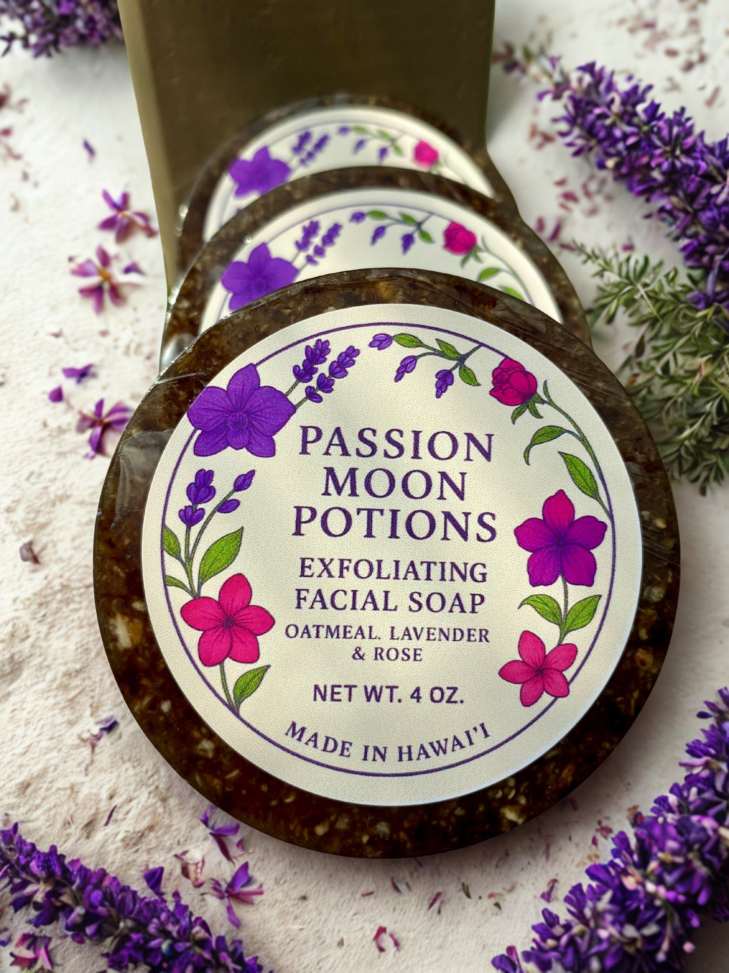 Exfoliating facial soap from Passion Moon Potions surrounded by lavender flowers on a light background.